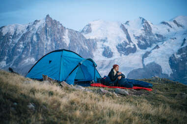 hiker sitting near tent in snowy mountains