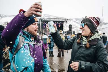 two people in snow cheersing with beers