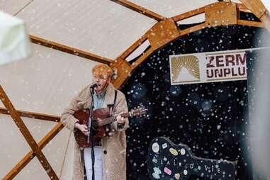 a man with a guitar playing in a tent in the snow